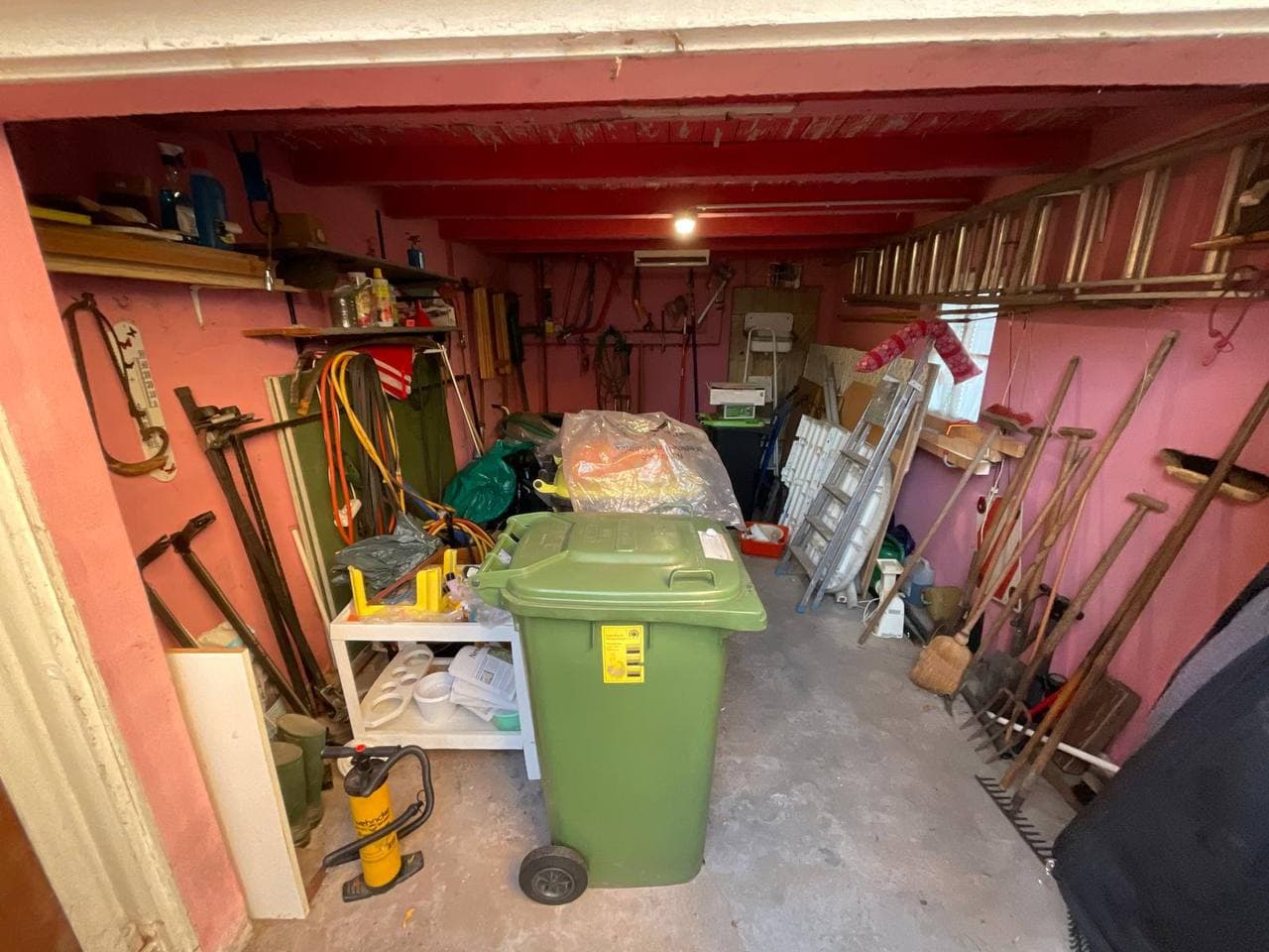 Volle Garage mit Gartengeräten, Leiter und Mülltonne
